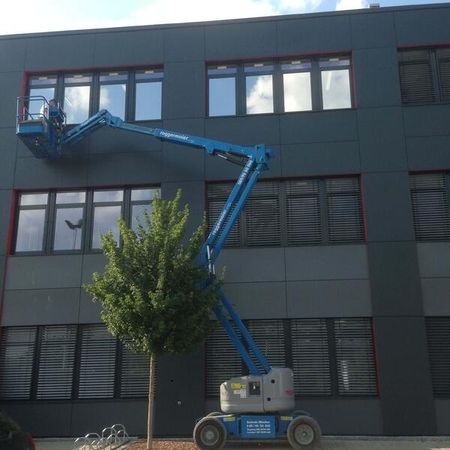 Ein blauer Kran steht vor einem Gebäude mit folierten Fenstern